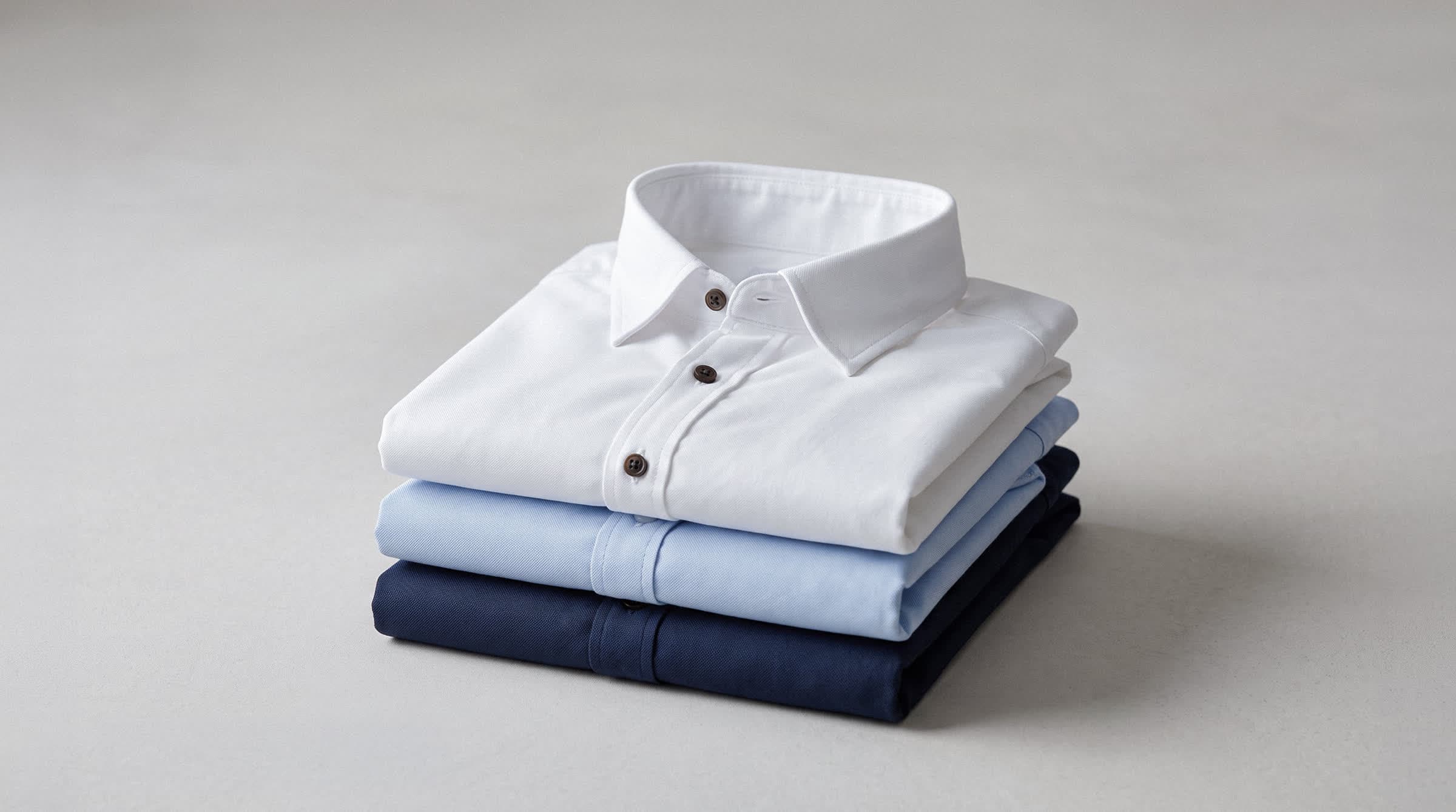 Tres camisas dobladas y apiladas en blanco, celeste y azul marino sobre una superficie clara